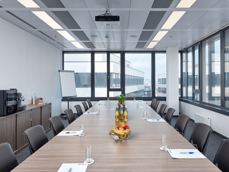 Heller und moderner Konferenzraum mit einem großen Holz-Besprechungstisch, ergonomischen Stühlen, Beamer und großen Fenstern mit Stadtblick.