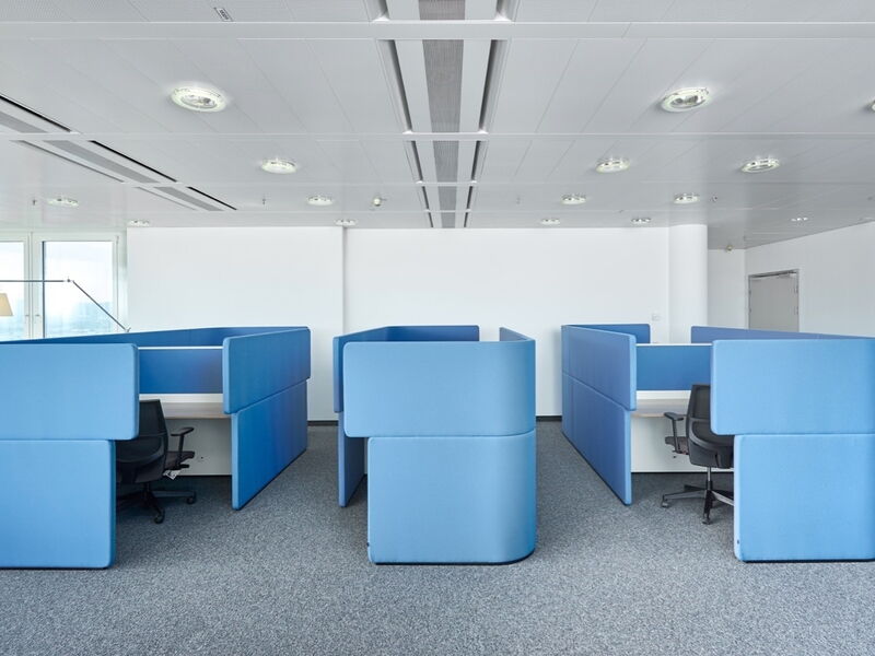 Modernes Großraumbüro mit blauen Akustik-Raumteilern, Sichtschutz-Kabinen und ergonomischen Bürostühlen auf grauem Teppichboden.