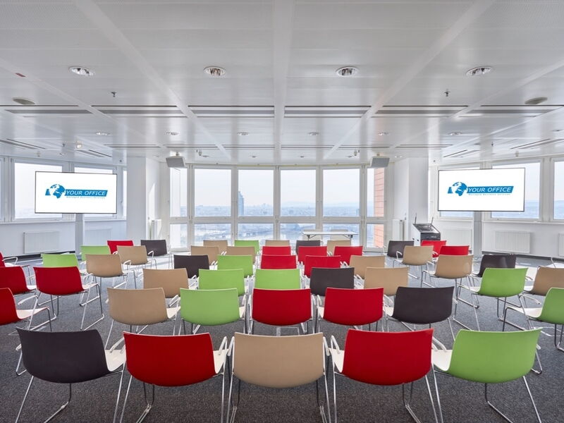 Geräumiger, moderner Firmenkonferenzraum mit bunten Stühlen und großen Bildschirmen mit 'Your Office'-Logo sowie Panoramablick auf die Stadt durch große Fenster.
