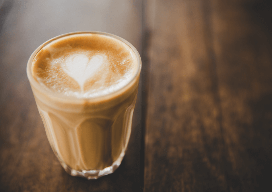 A glass of fresh cappuccino with delicate heart-shaped latte art sitting on a rustic wooden table