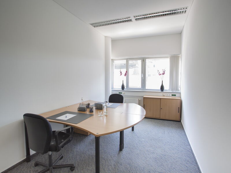 Helles Büro mit großem Holztisch, schwarzen Bürostühlen und einem Fenster mit Tageslicht.