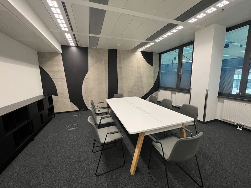 Heller Büro-Konferenzraum mit einem langen weißen Tisch, grauen Stühlen und einer dekorativen schwarz-beigen Akzentwand
