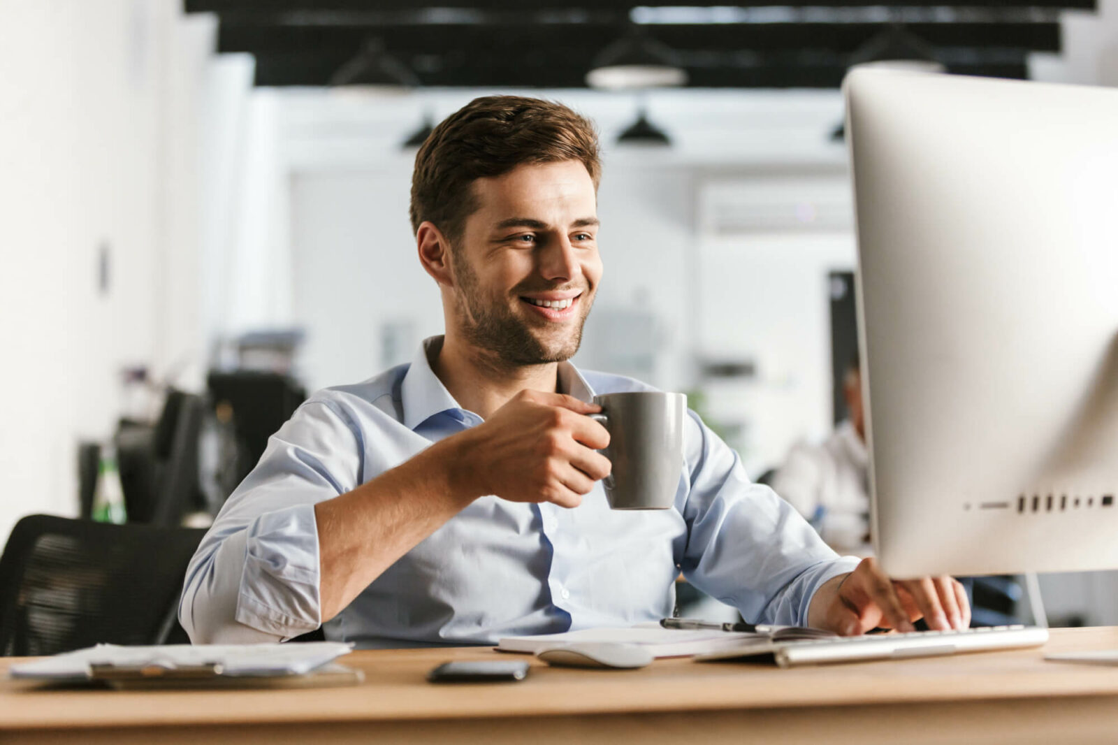 smiling-business-man-drinking-coffee-using-computer-while-sitting-by-table-office